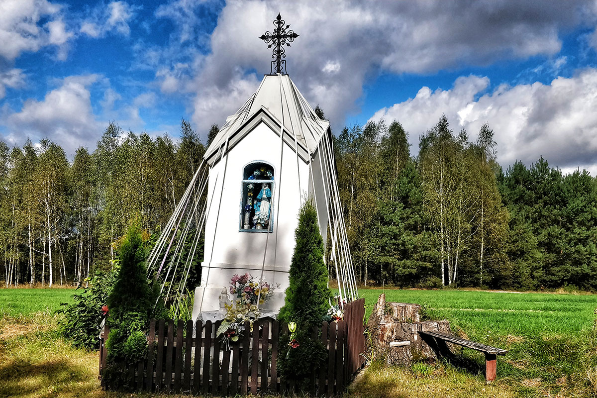 Outdoor shrine, like a miniature church, surrounded by ribbons, picket fence, and shrubs.