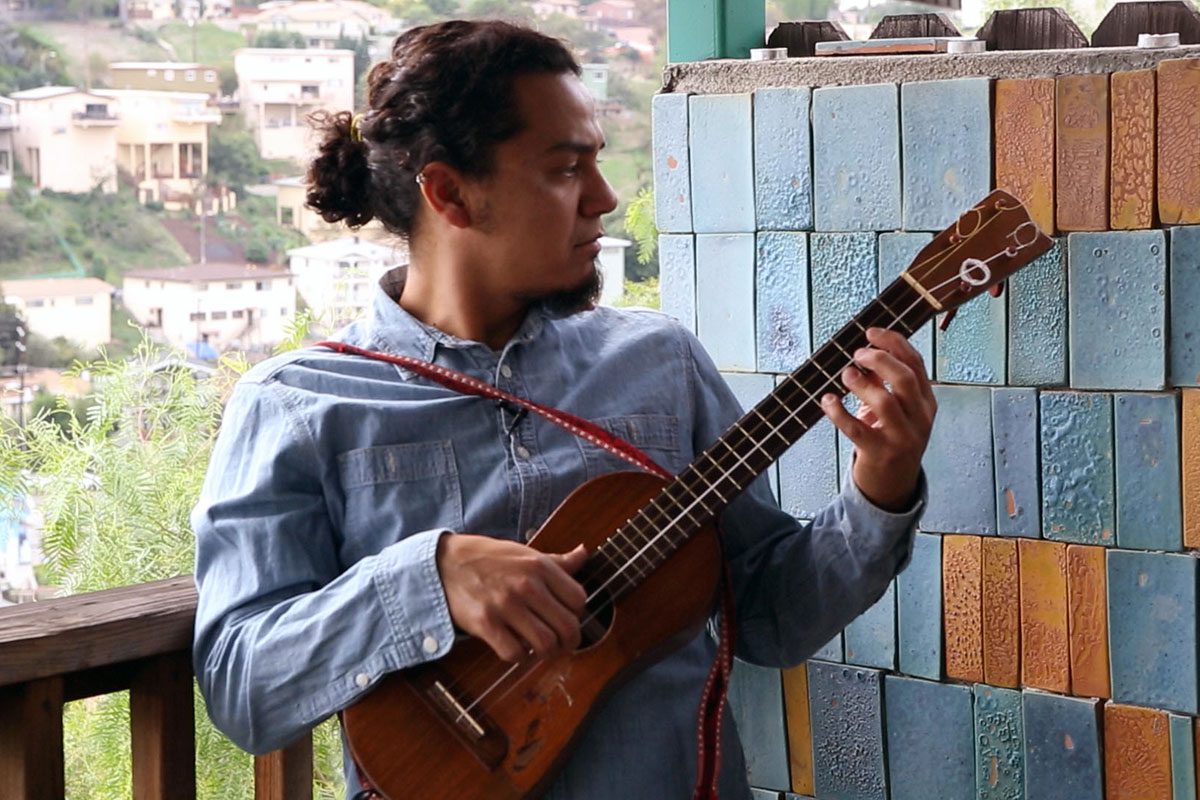 A man holds up and plucks a jarana (small stringed instrument).