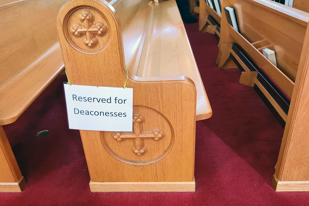 On the side of a wooden church pew, a printed sign reads, Reserved for deaconesses.