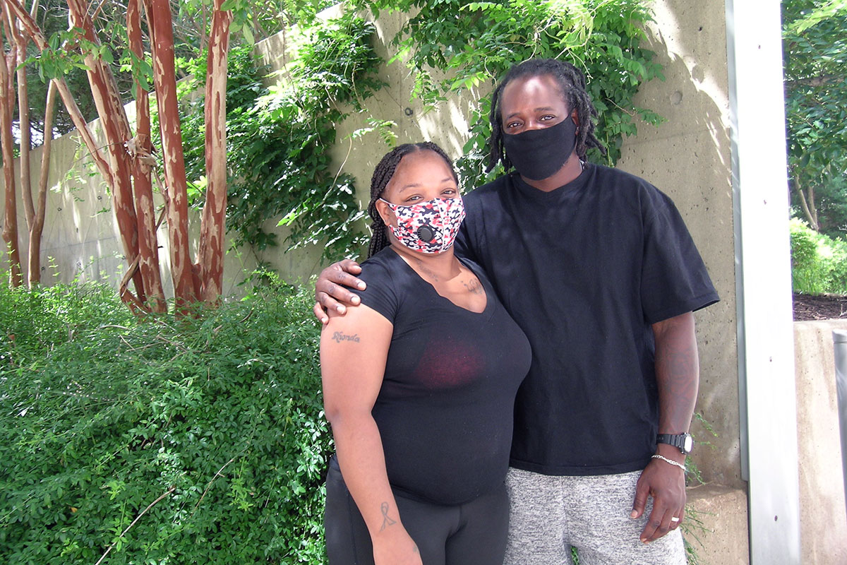 A Black couple stands outside an office building, arm in arm, face masks on.
