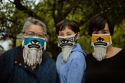 Three people, three generations of a family, pose outdoors wearing decorative beaded face masks.