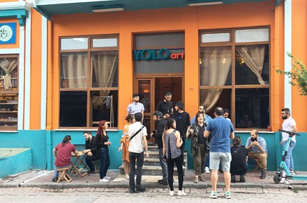 A crowd of people stand outside a bright orange building.