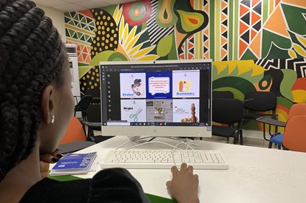 A woman at a computer is looking at images of educational language content with a colorful mural in the background.