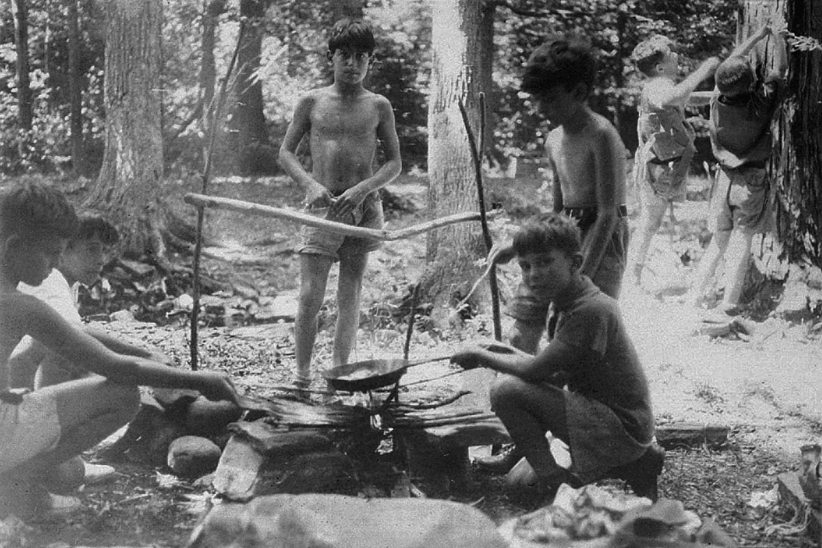 Black-and-white photo of a group of young boys preparing a meal over a fire pit at Camp Boiberik in the summer of 1936