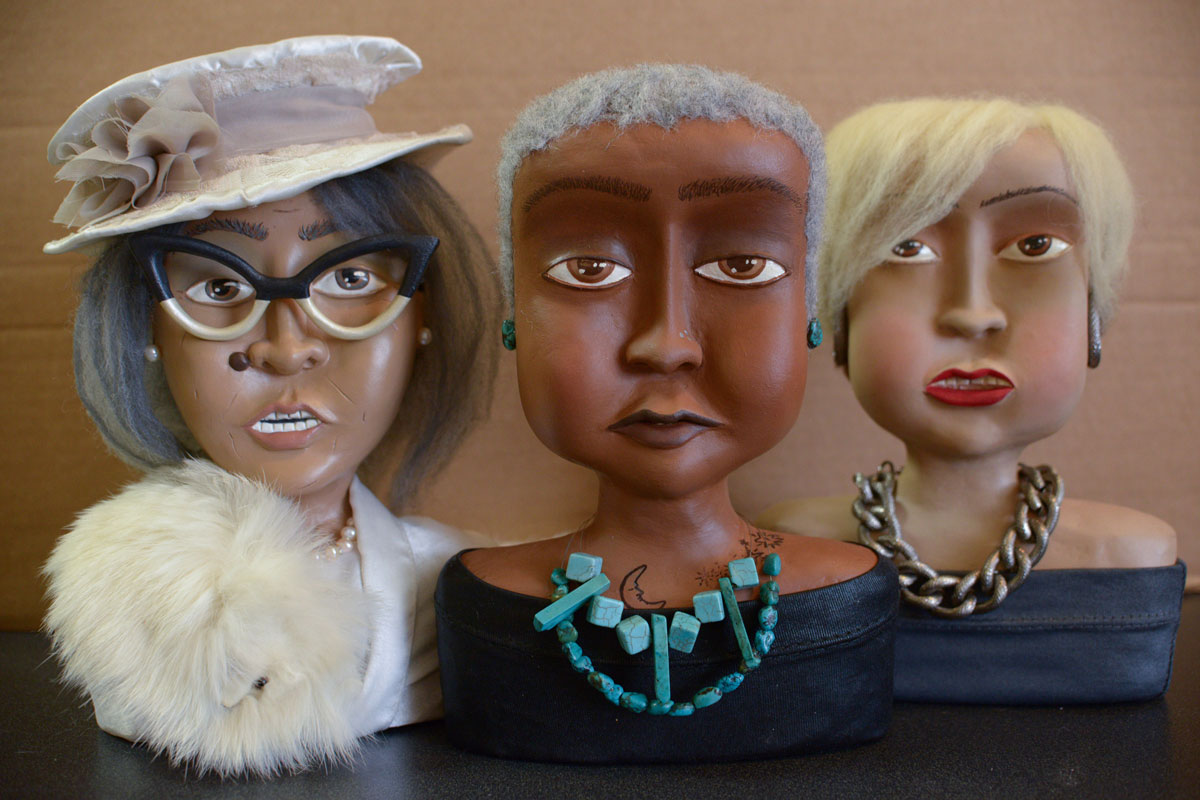 Three older black female dolls each wearing an assortment of accessories. 