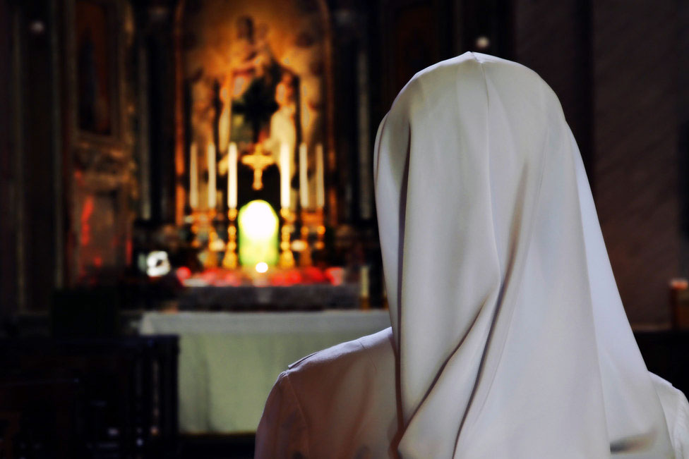 From behind, a person in a white veil faces a Catholic altar.