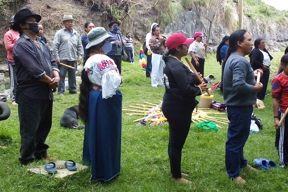 People gather in a circle, partly socially distanced, around an offering in the grass.