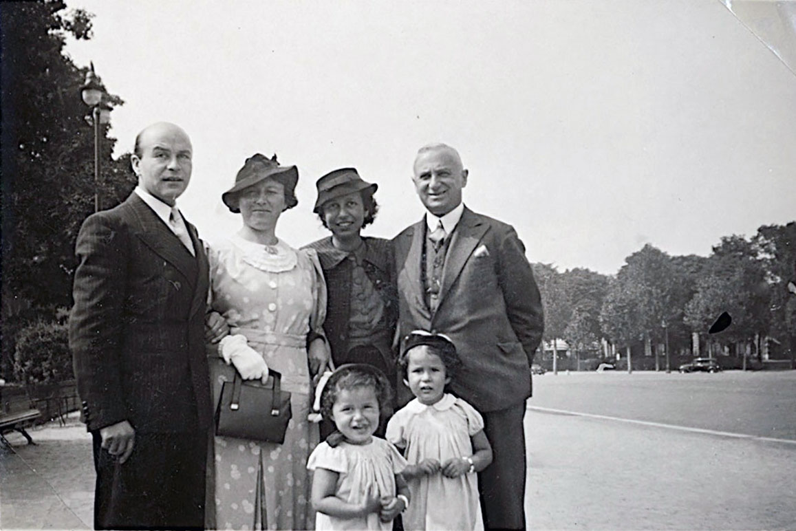 Four adults and two young children, all dressed in formal wear, pose together outdoors. Black-and-white photo.