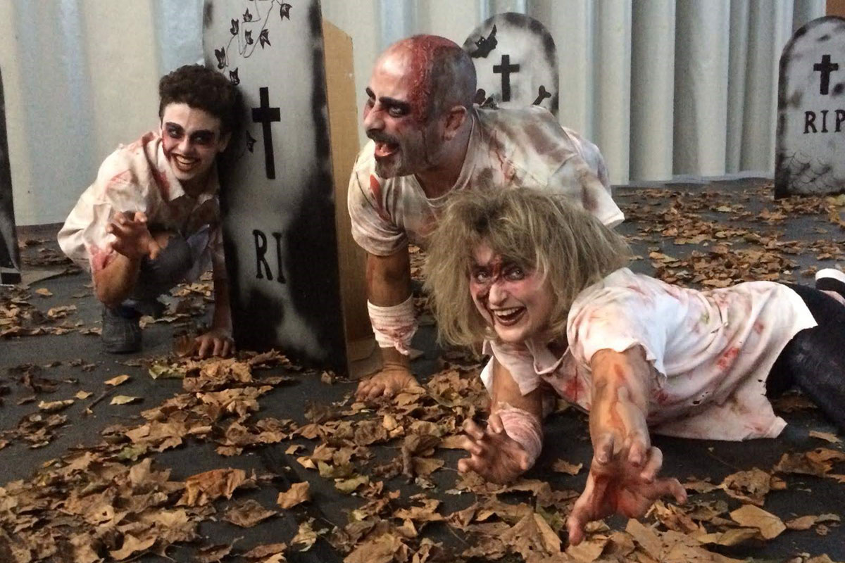 Tres persones fan de zombis esquitxades de sang en un carrer ple de fulles mortes i làpides de cartró.