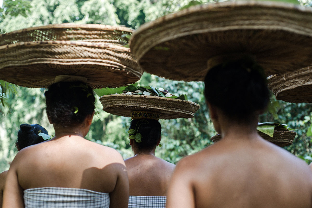 From behind, several women balance short but wide baskets on their heads. 