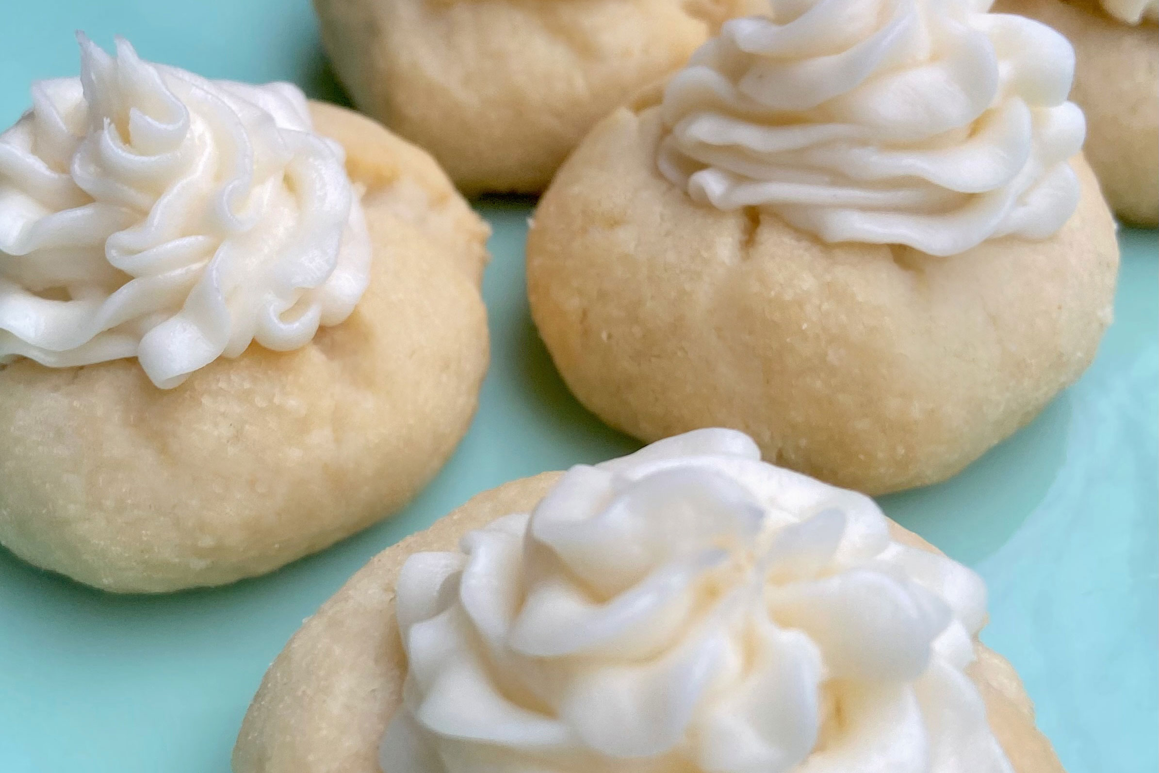 Pale cookies topped with a swirl of pale white frosting on a turquoise plate.