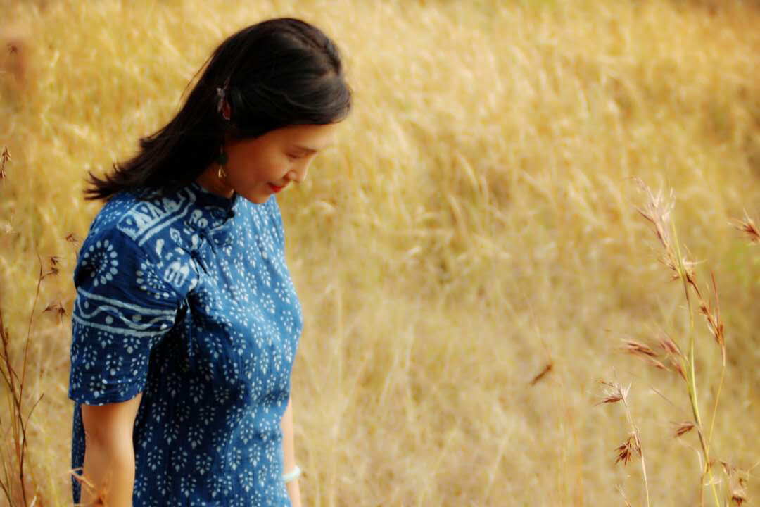 A woman walks through a field a golden grass wearing an indigo-dyed dress.