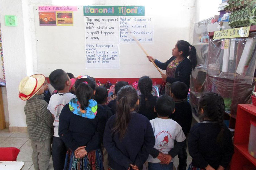 A teacher points to words on the board in front of a classroom of young students.