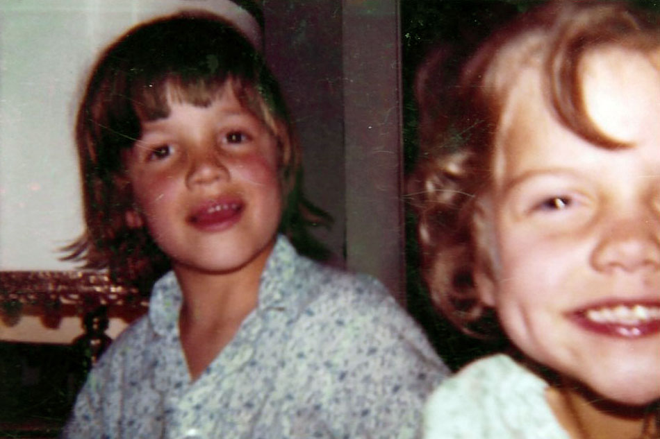 Blond-haired boy and girl smile for the camera. Faded color photo.