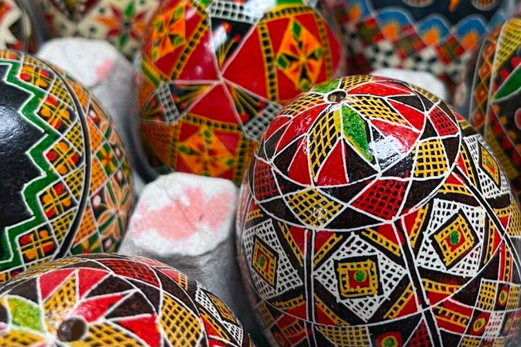 Several eggs with intricate geometric patterns dyed in black, red, white, yellow, and green, resting in a gray cardboard carton.