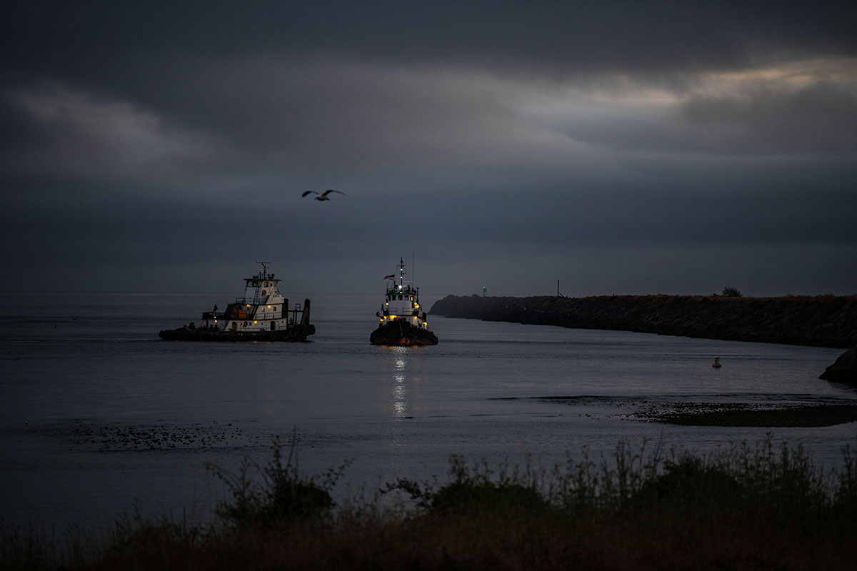 Two fishing boats near a shoreline at dusk. 