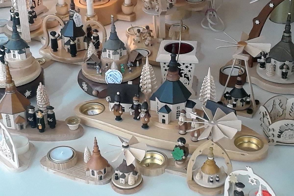 A display of wooden toys that seem to form a village: steepled churches, evergreen trees, windmills, figures of people in uniform, all in natural blonde wood and earthen tones.