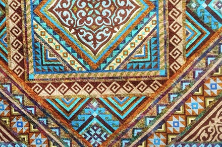Closeup on a quilt with geometric patterns in blue, brown, tan, and aqua. 