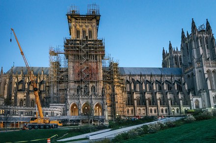 Against a dusky dark blue sky, the National Cathedral stands blocked by extensive scaffolding and a tall yellow crane. 