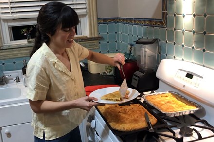 A woman holds up a piece of chicken pie, with the remainder next to her on the stove.