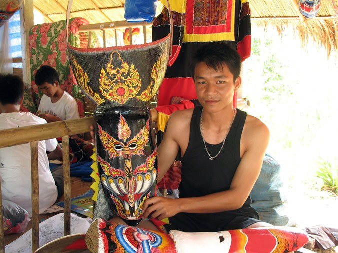At work in Thailand, Wirayut Natsaengsri shows a Phi Ta Khon mask he made with another one in the works in his lap. Photo by Sunee Prasongbandit, Ralph Rinzler Folklife Archives