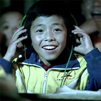 A child holds his hands up to the headphones over his ears, looking elated.